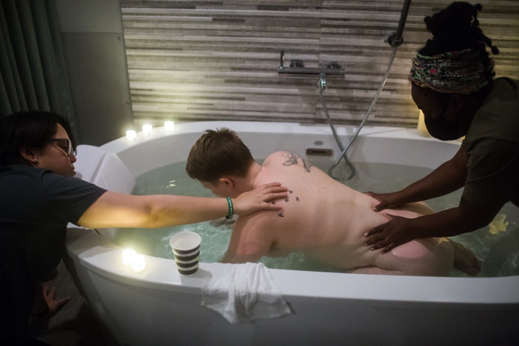 birthing person in tub with supportive hands on back